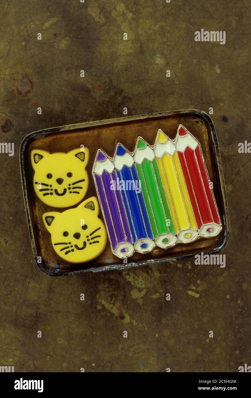Kleiner Messingdeckel mit Emaille Brosche oder Abzeichen oder Stift von geschärften Farbstiften und zwei Kunststoff lächelnde Katzengesichter Stockfoto