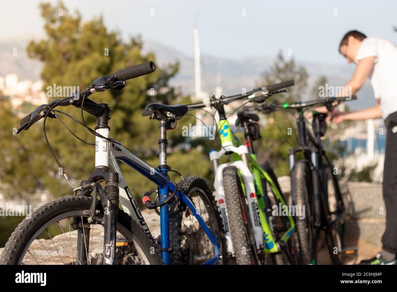 Split, Kroatien Mai 2020 Blaugrüne und schwarze Mountainbikes stehen an einer Wand. Scott und Cube Marken beliebte Fahrräder, Mann fiddling mit dem letzten Fahrrad. Stockfoto