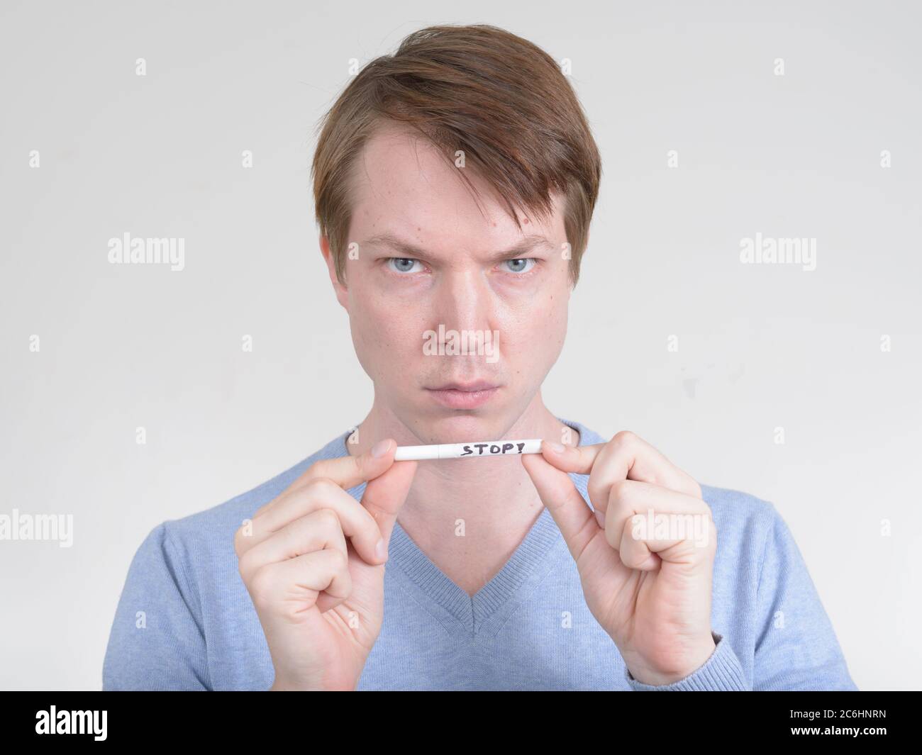 Porträt eines jungen Mannes, der ernst aussieht, während er die Zigarette mit STOPPSCHILD hält Stockfoto