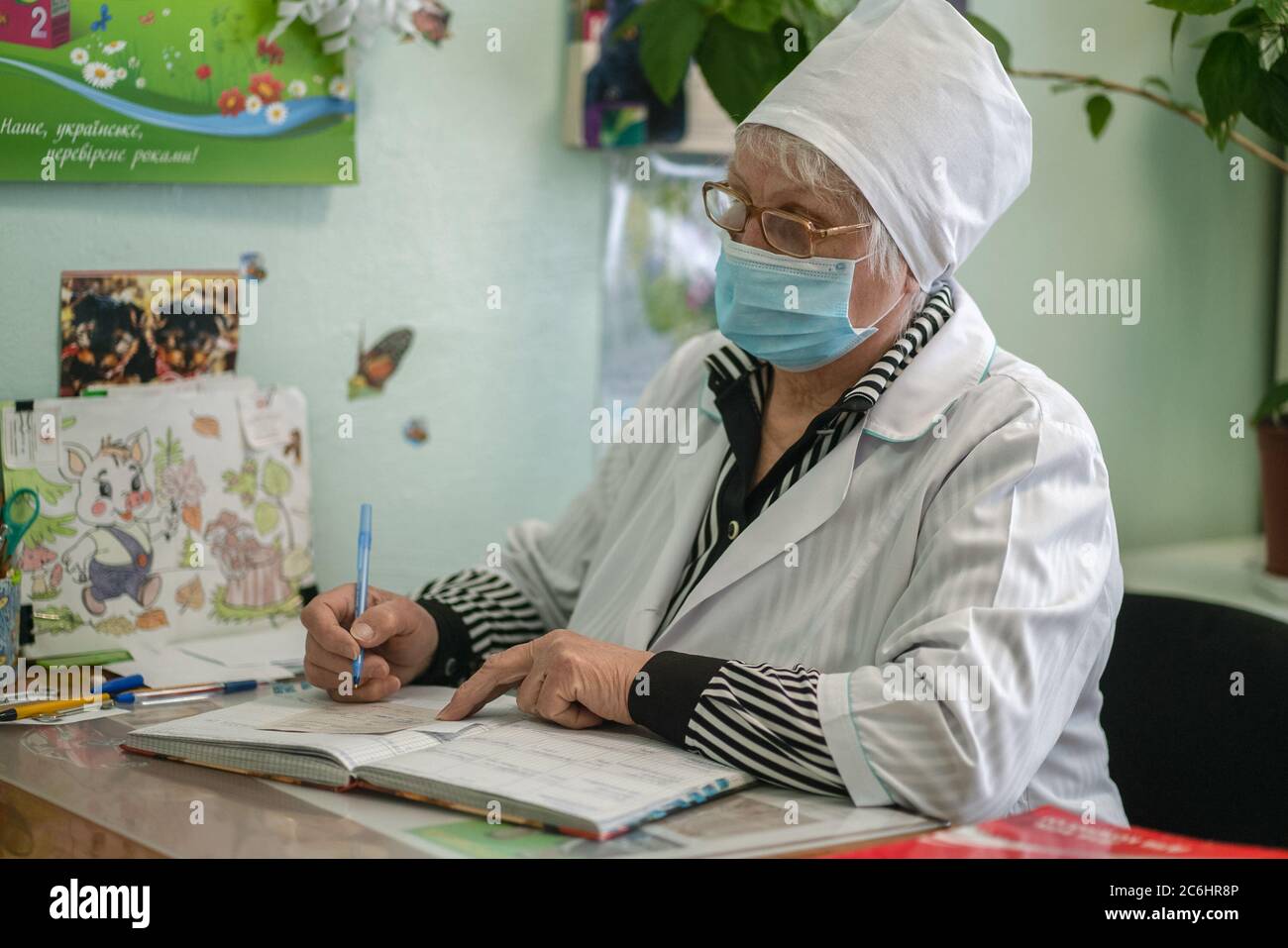 Ältere Krankenschwester verschreibt ärztliche Verschreibung für den Patienten. Maskierte ältere Frau schreibt in der Patientenkarte. Stadtkrankenhaus. Mai 2020, Brovary, Ukraine Stockfoto
