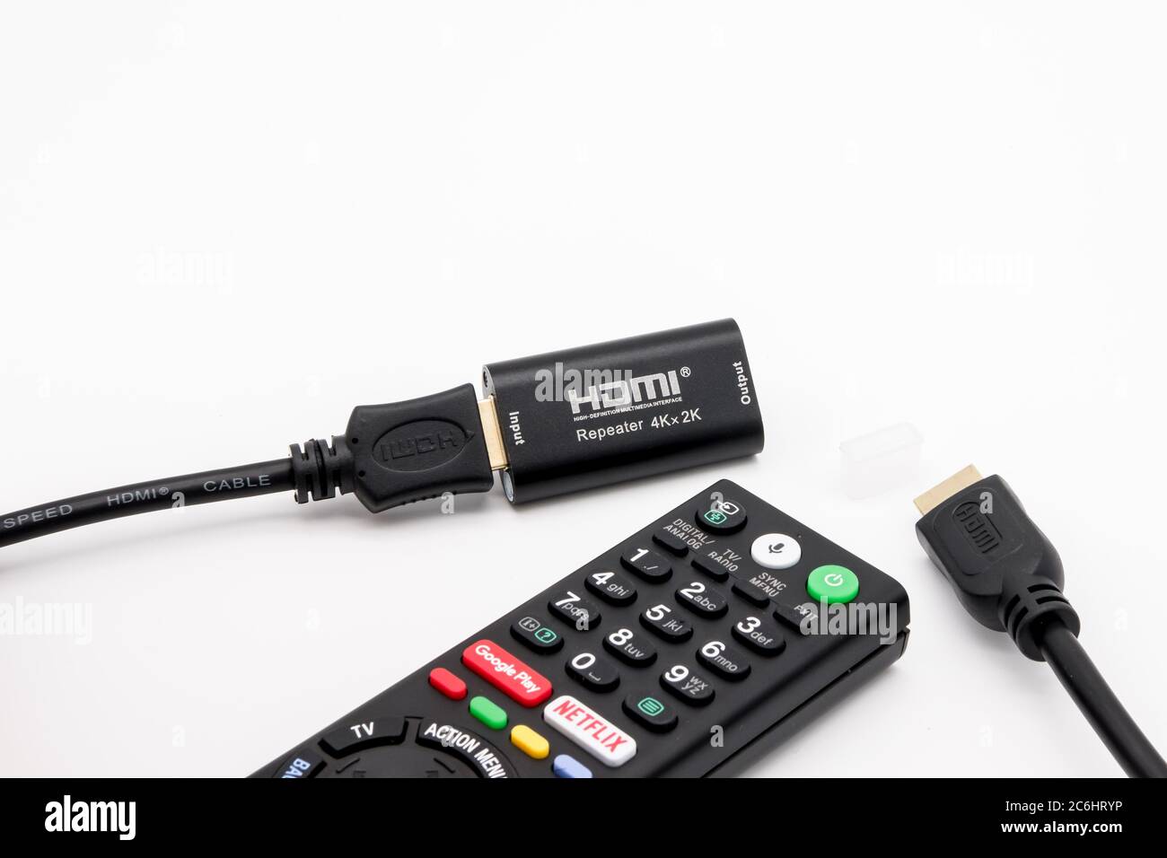 Nahaufnahme einer 4K-fähigen TV-Fernbedienung, die neben HDMI-Kabeln zu sehen ist, die selbst mit einem HDMI 4K-Signalverstärker verbunden sind. Stockfoto