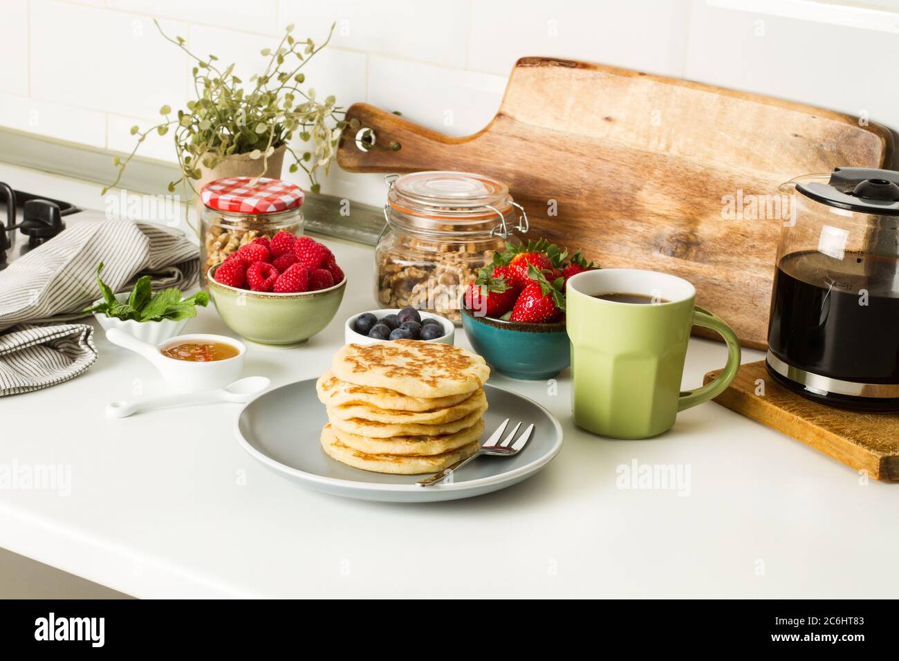 Pfannkuchen mit Beeren und Honig auf einem grauen Teller und mit einer Tasse Kaffee auf einer Küchentheke Stockfoto