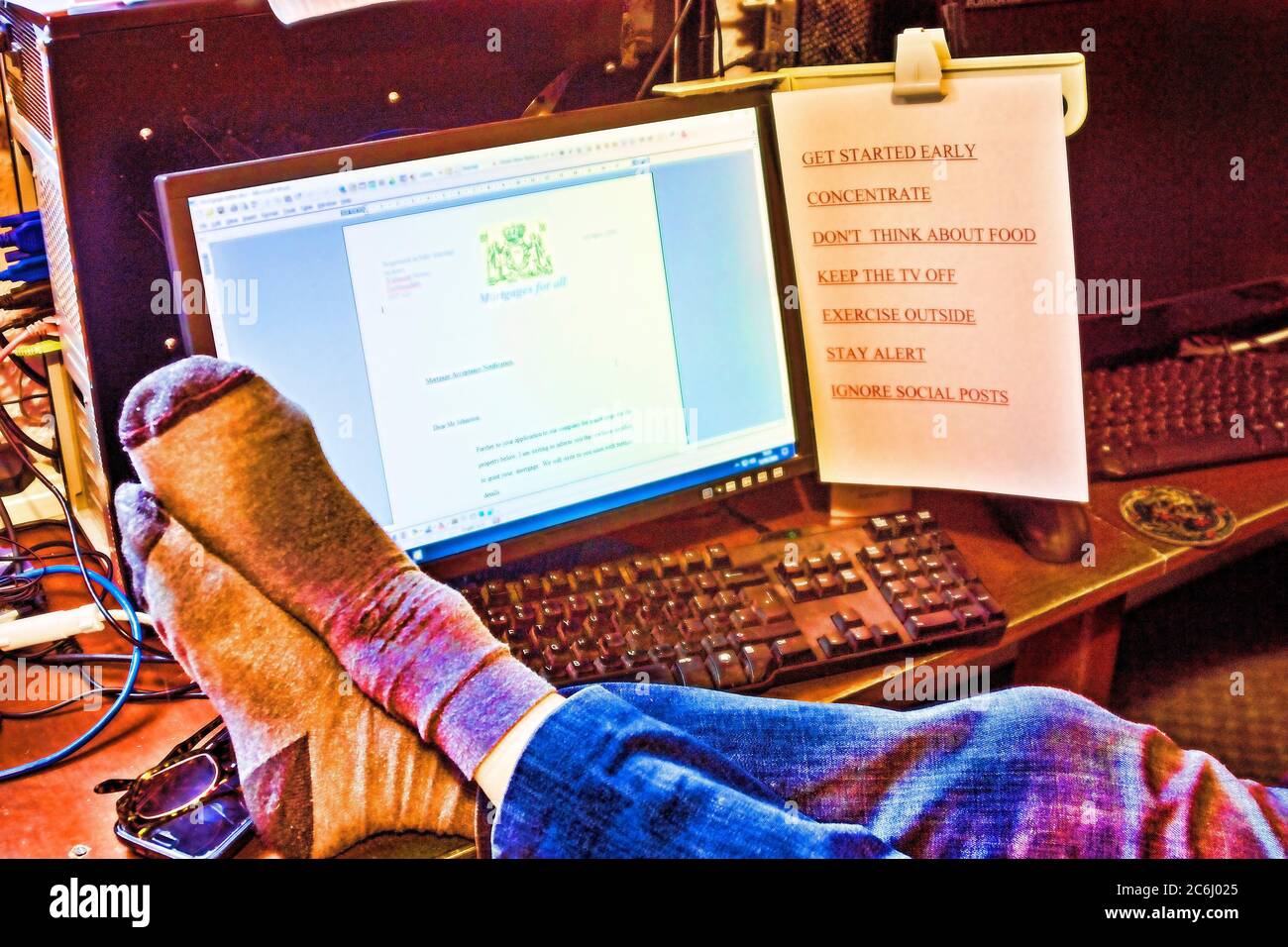 Arbeiten von zu Hause aus. Konzept-Image. Covid 19 Coronavirus. Computer, Anweisungen, Füße am Schreibtisch. Computerbildschirm mit imaginären, fiktiven, cr Stockfoto