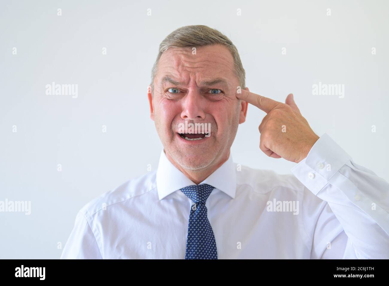 Besorgter Mann mit einem angstlosen hoffnungslosen Ausdruck macht eine Pistole Geste zeigt auf seinen Kopf mit seiner Hand Konzept der Selbstmordgedanken in einem Kopf und Stockfoto