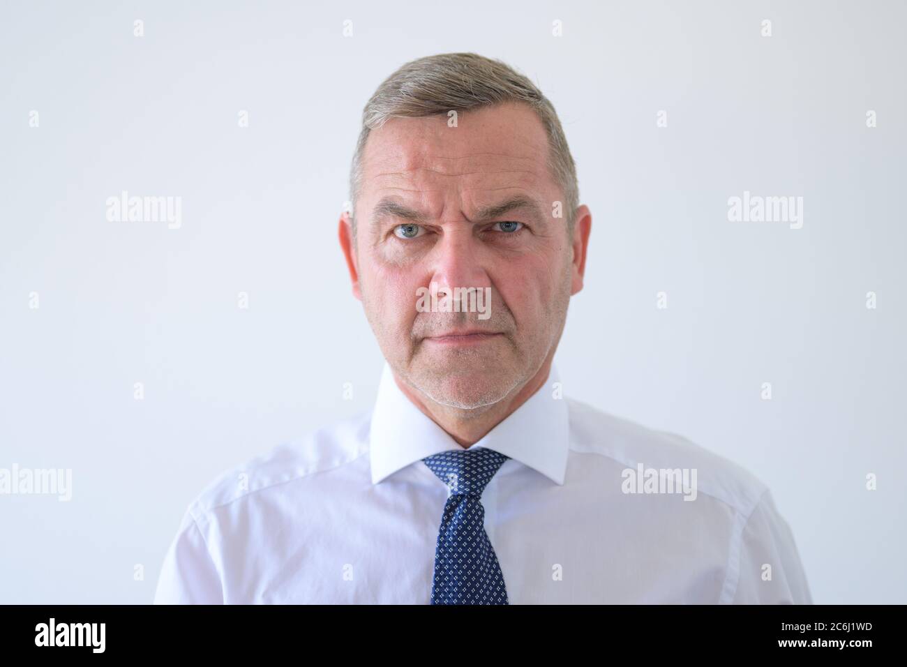 Scharfsinniger Mann, der der Kamera einen einfühlenden Blick mit einem leichten Stirnrunzeln der Konzentration in einem Kopf- und Schulterporträt auf Weiß verleiht Stockfoto