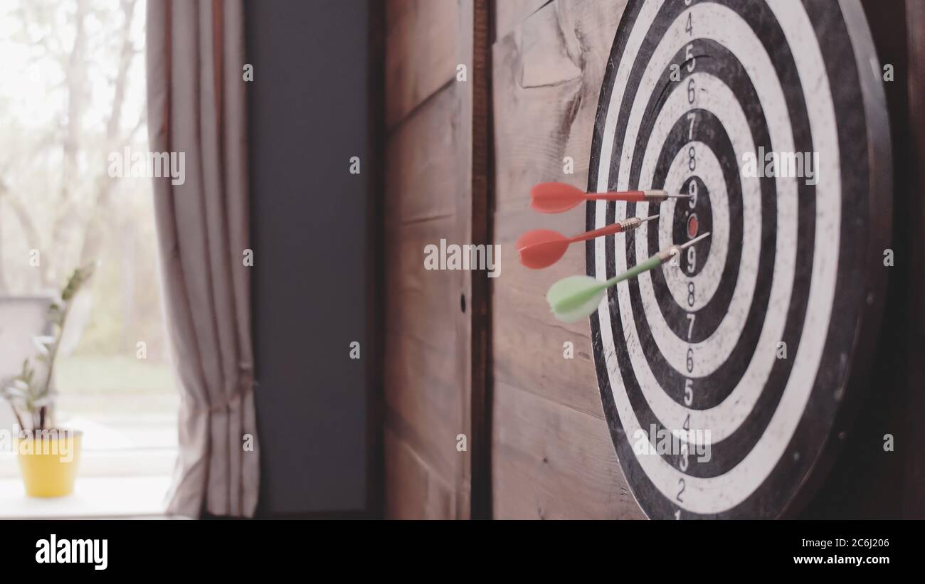 Drei Darts Pfeile treffen das Bullseye. Dartscheibe, die an einer Holzwand von zu Hause oder im Büro hängt. Ziel- oder Zielkonzept erreichen. Nahaufnahme. Getöntes Bild Stockfoto