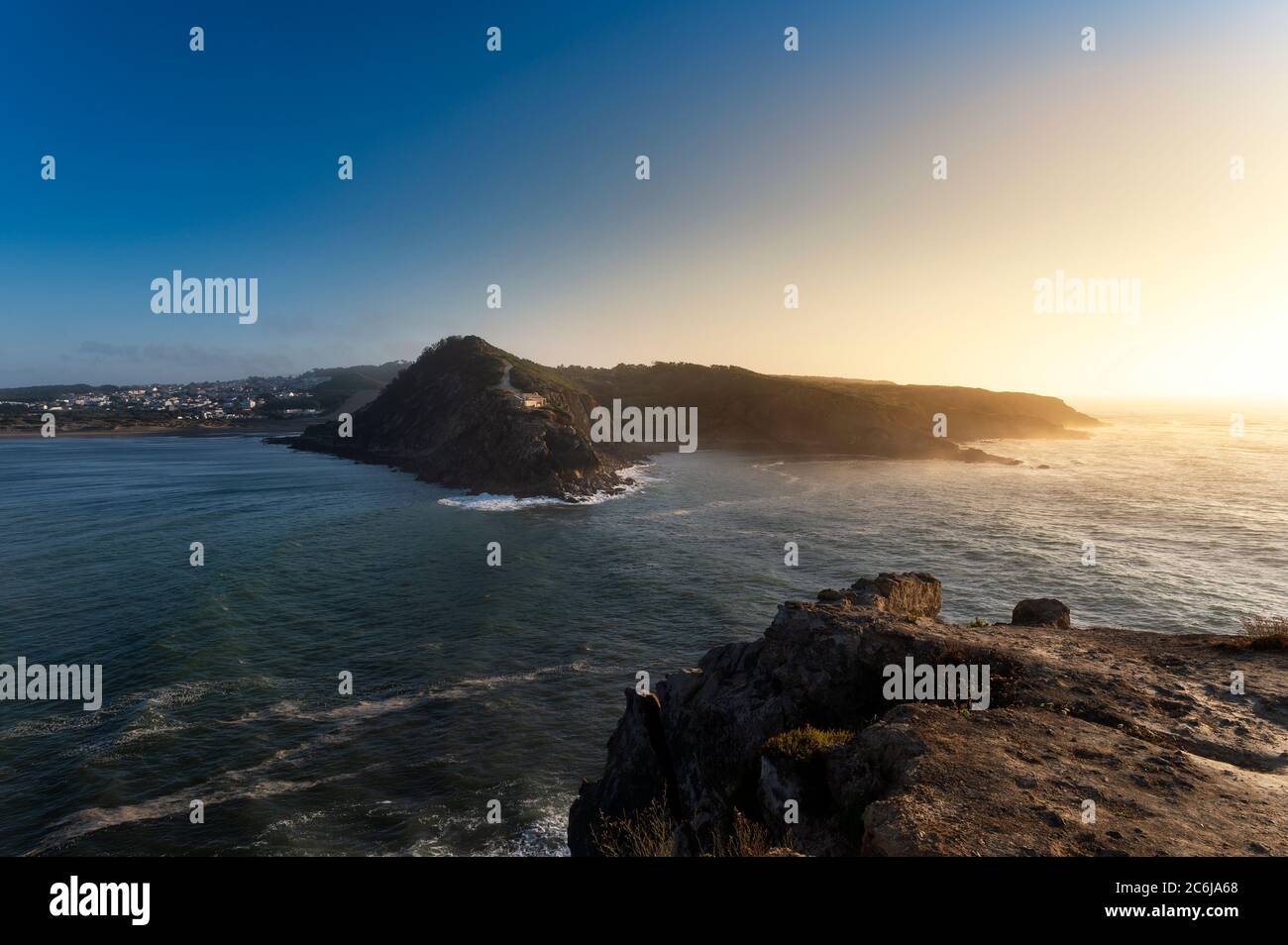 Blick auf die Landzungen am Eingang der Bucht São Martinho do Porto, mit dem Leuchtturm, bei Sonnenuntergang. Stockfoto