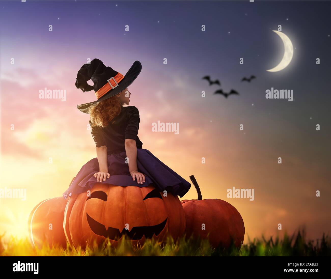 Frohe Halloween! Niedliche kleine Hexe mit einem großen Kürbis. Schöne junge Mädchen im Hexenkostüm im Freien. Stockfoto