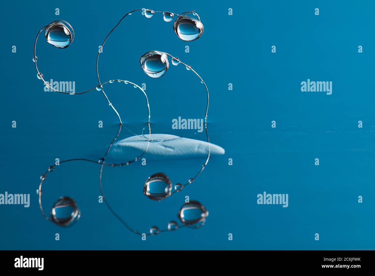 Wassertropfen hängen an gebogenen dünnen Metalldrähten, die vor blauem Hintergrund über der Oberfläche aus dem Wasser ragen. Stockfoto