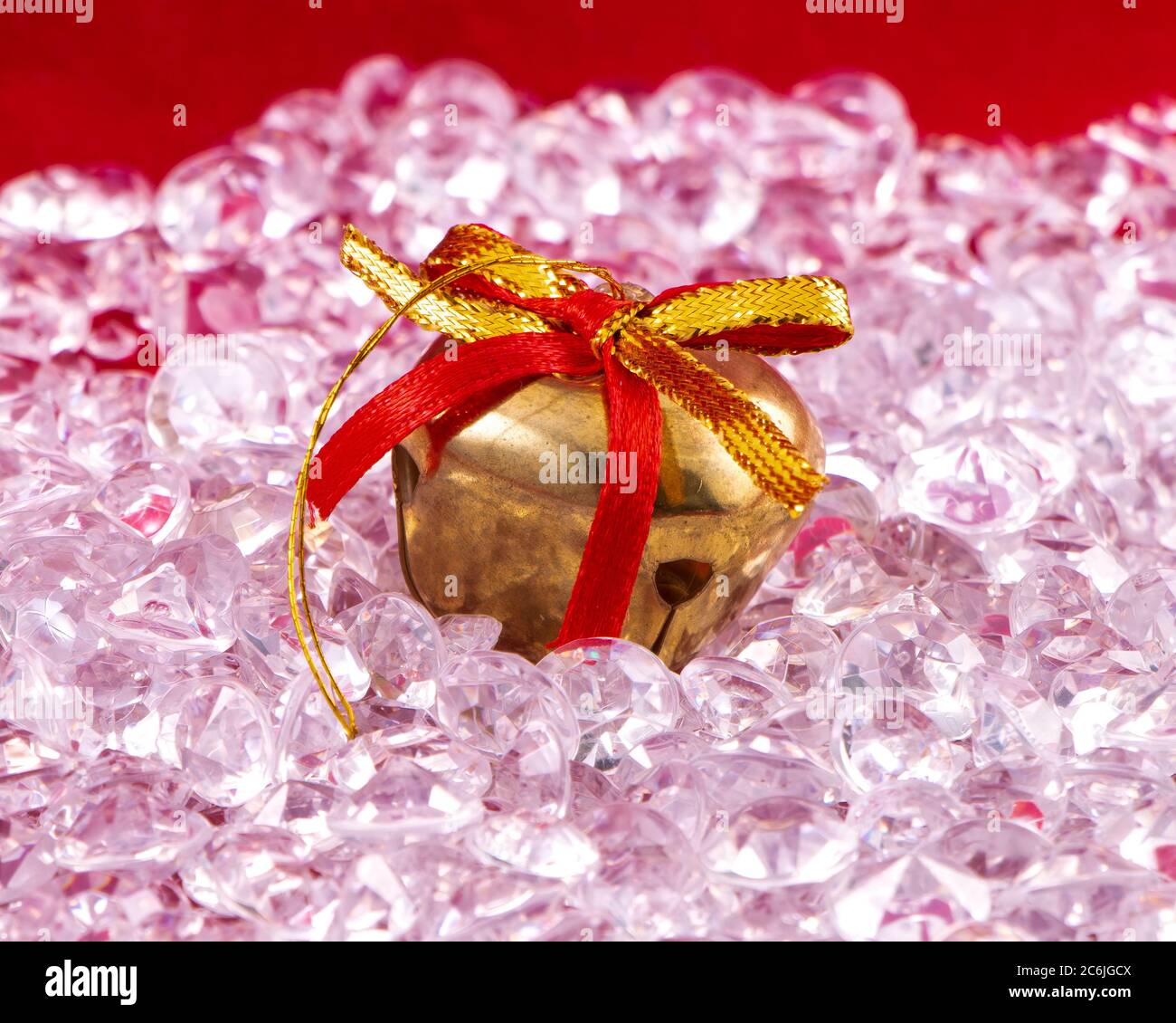 Nahaufnahme der Weihnachtsglocke mit roten und goldenen Bändern auf dem Bett aus Kristallen Stockfoto