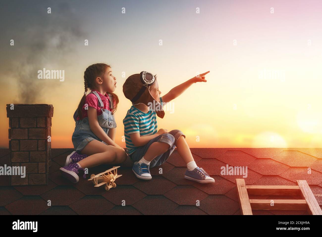 Zwei kleine Kinder spielen auf dem Dach des Hauses und schauen in den Himmel und träumen davon, Pilot zu werden. Stockfoto