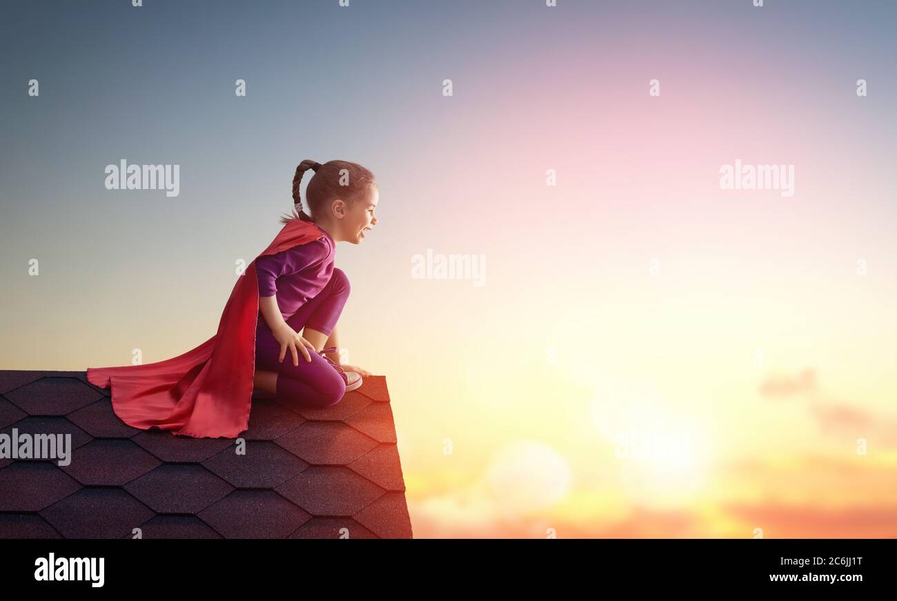 Kleines Mädchen spielt Superheld. Kind auf dem Hintergrund des Sonnenuntergangs Himmel. Mädchen Power Konzept Stockfoto