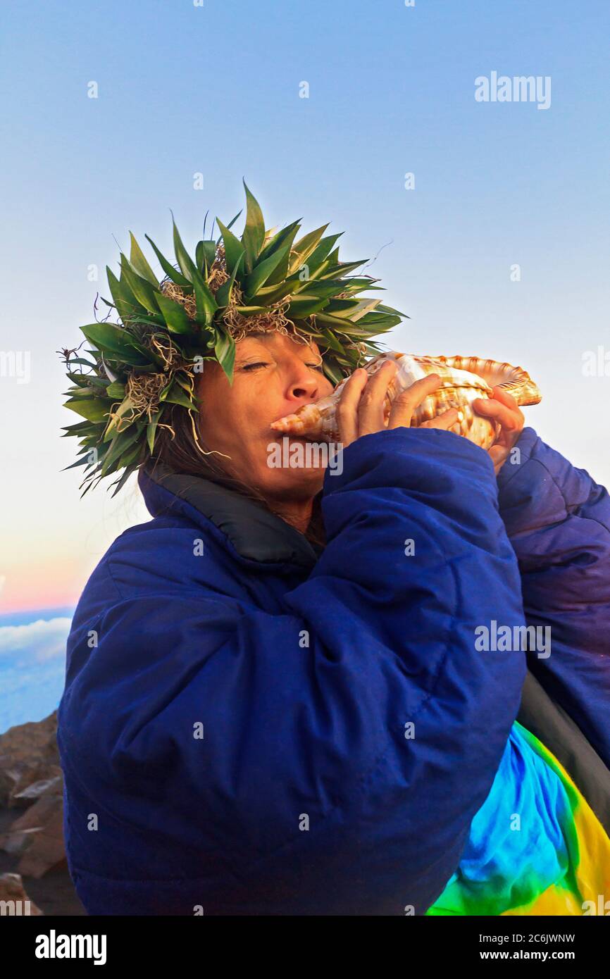 Barbara Bohonu, spirituelle/kulturelle Heilerin, begrüßt den Sonnenaufgang mit einem Gesang und bläst eine Muschelschale am Haleakala Krater, Maui, Hawaii, USA. Stockfoto