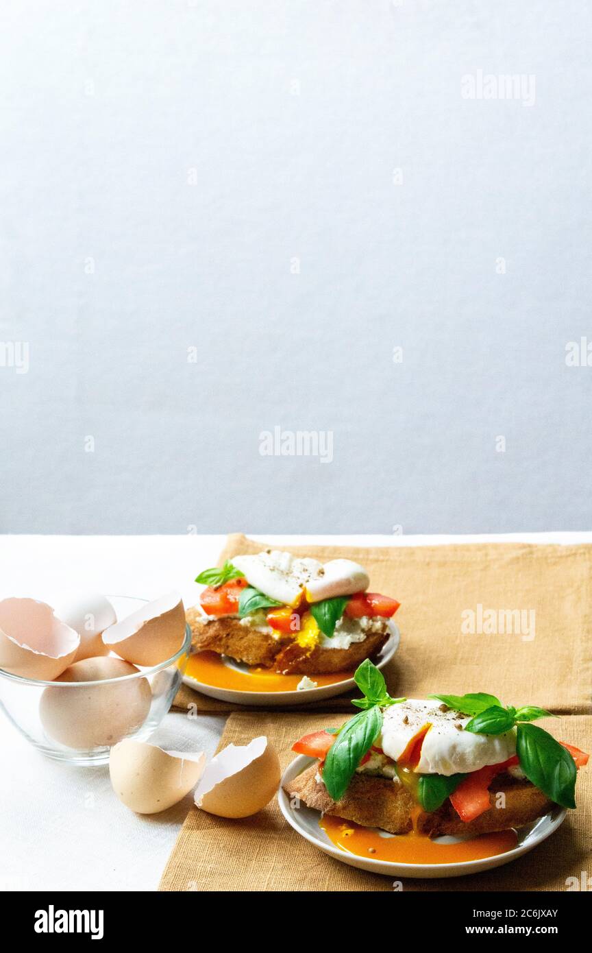 Leckere Sandwiches mit Basilikum, Tomaten und pochierten Eiern auf dem Teller Stockfoto