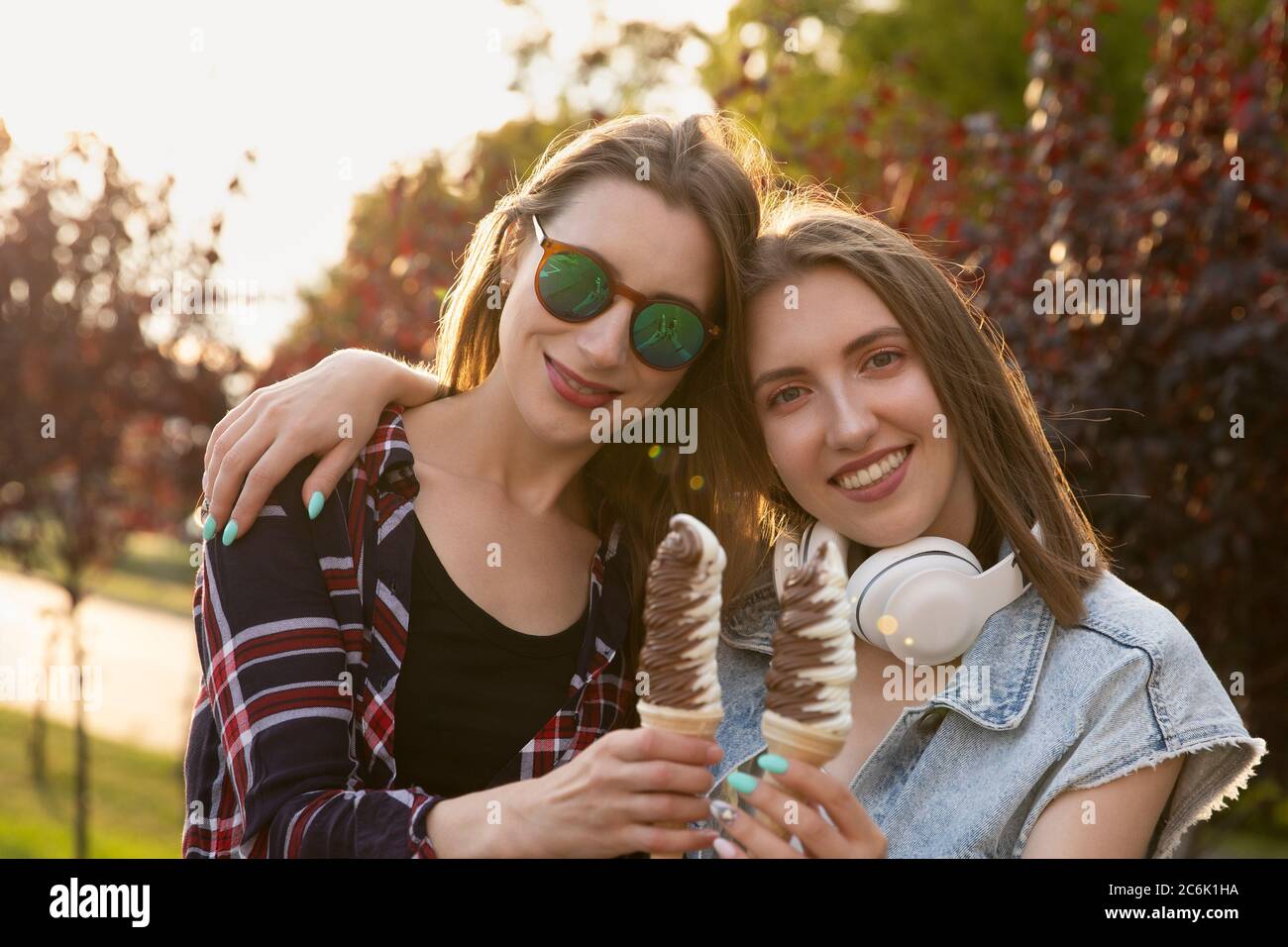 Zwei junge Mädchen gehen und essen Eis im Glas. Freundinnen genießen Nachtisch, sie haben Spaß und entspannen sich an der frischen Luft. Stockfoto