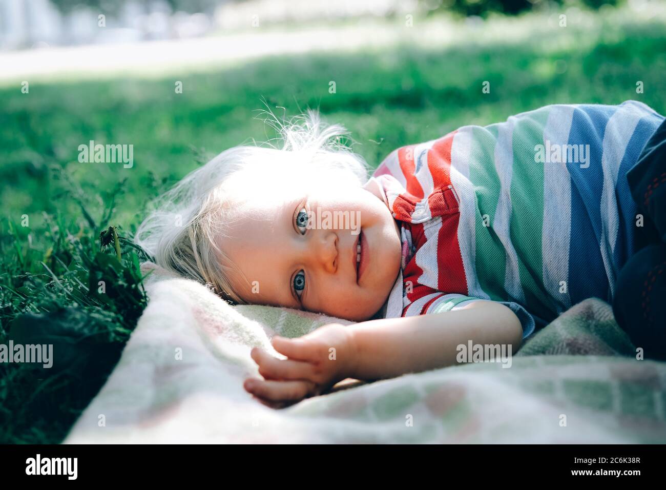 Porträt eines süßen glücklichen kleinen Jungen mit blonden Haaren und blauen Augen, im Gras im Park und lächelnd. Zurück zum normalen Konzept. Stockfoto