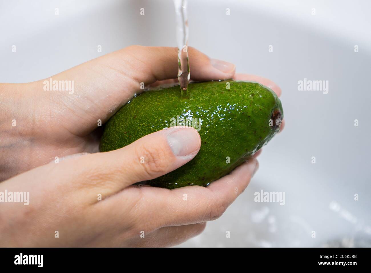 Waschen von Früchten unter fließendem Wasser. Hände und Avocado unter einem  Wasserstrom Stockfotografie - Alamy