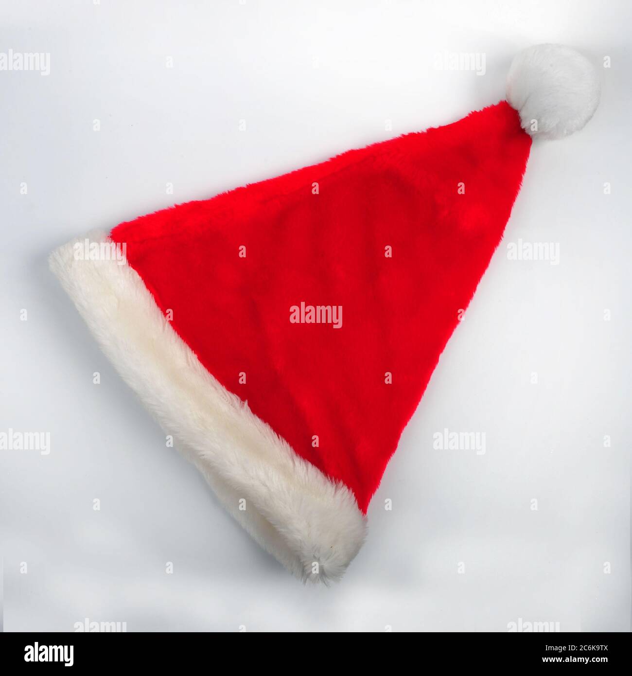 Weihnachtsmann Hut auf weißem Hintergrund mit Kopierraum im oberen und unteren Teil des Fotos. High-Winkel Schuss von roten Fuzzy Weihnachtsmütze diagonal platziert. Stockfoto