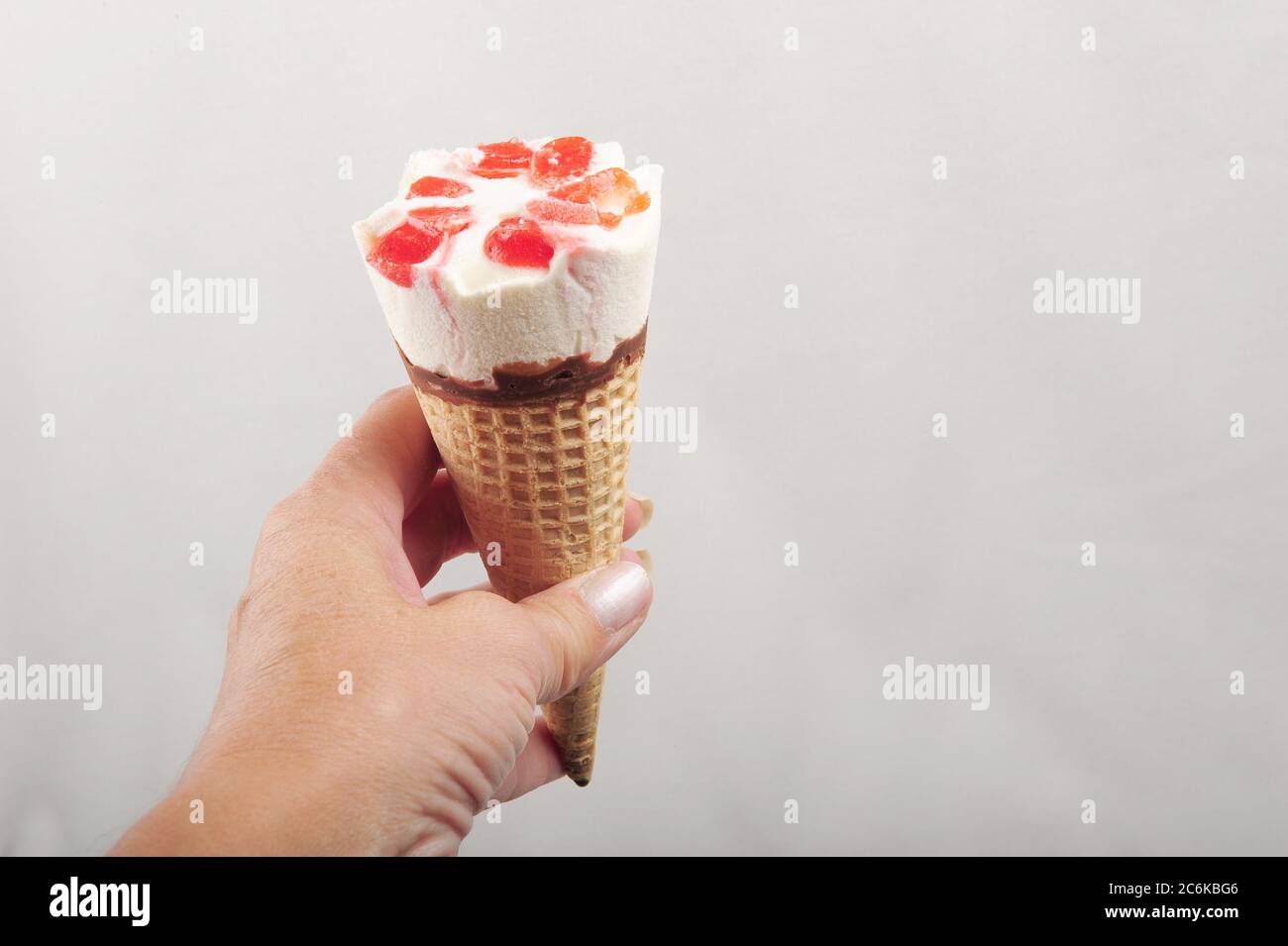 Hand hält Erdbeer Eis Kegel. Weißer Hintergrund mit Kopierfläche auf der rechten Seite. Horizontale Aufnahme. Stockfoto