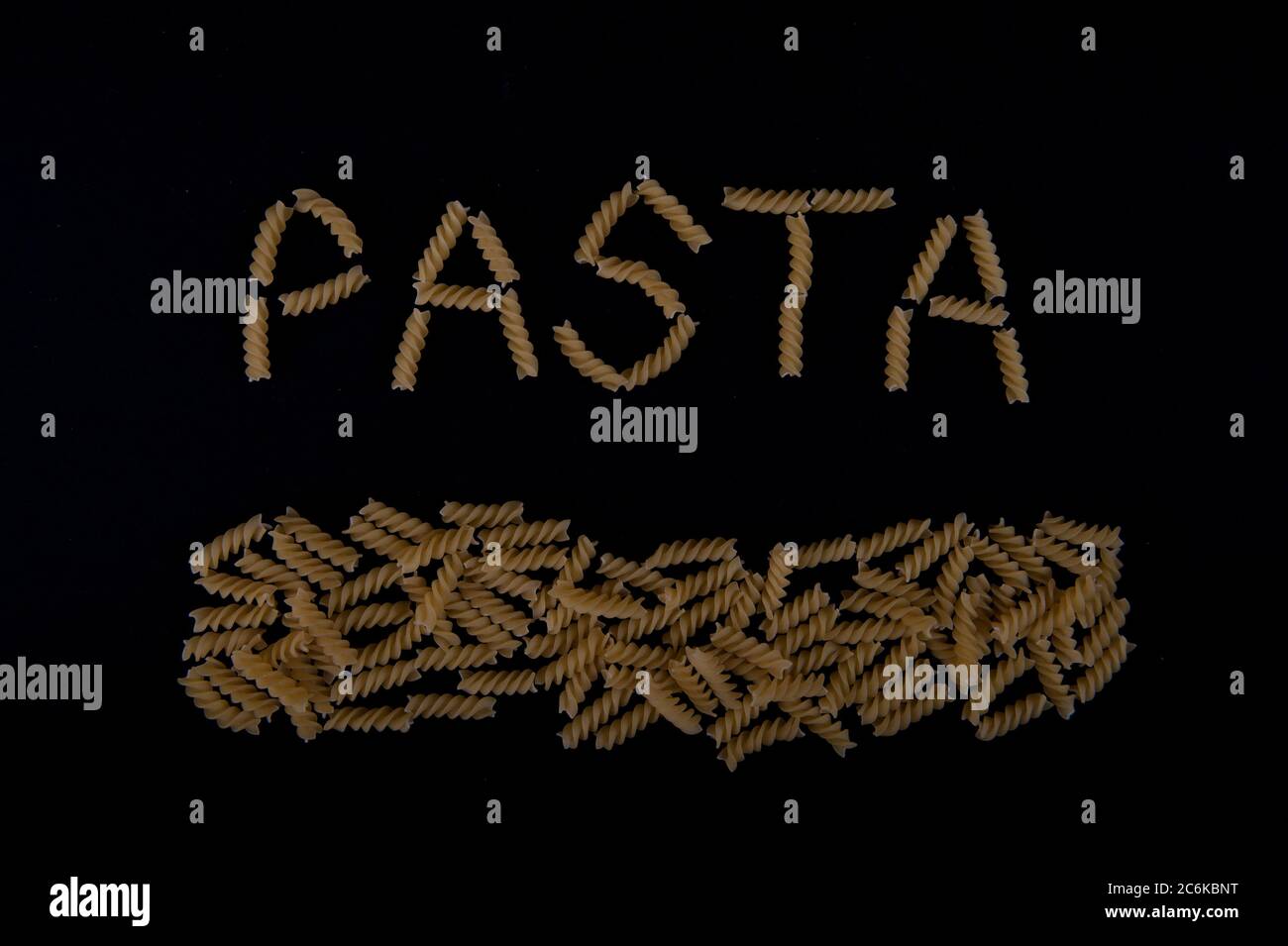 Das Wort Pasta mit Pastaschrauben geschrieben. Pasta entlang der unteren Teil des Bildes. Aufnahme mit hohem Winkel auf schwarzer Oberfläche. Stockfoto