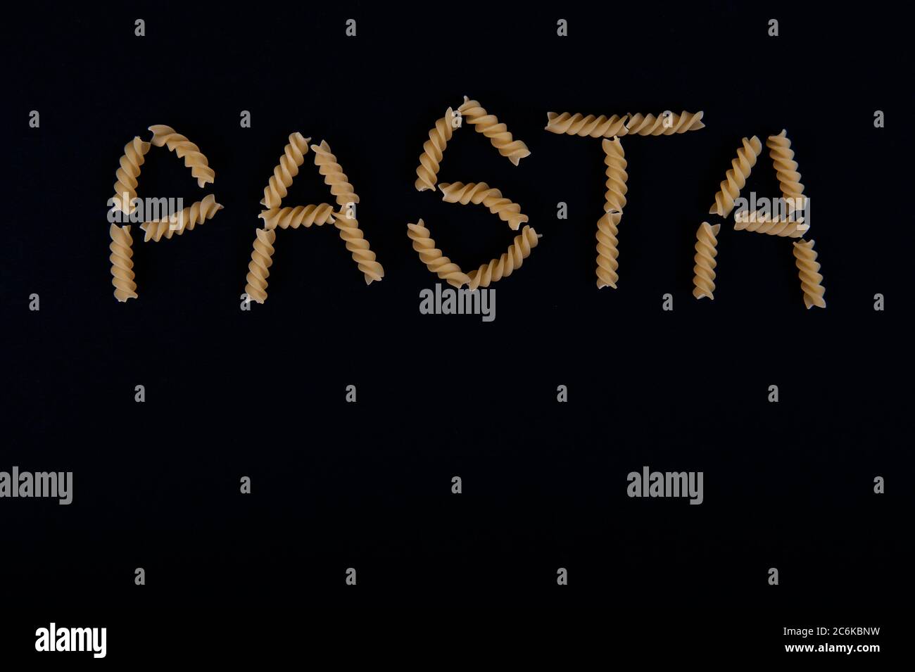 Das Wort Pasta mit Pastaschrauben geschrieben. Platz im unteren Teil des horizontalen Bildes kopieren. Schwarzer Hintergrund. Stockfoto