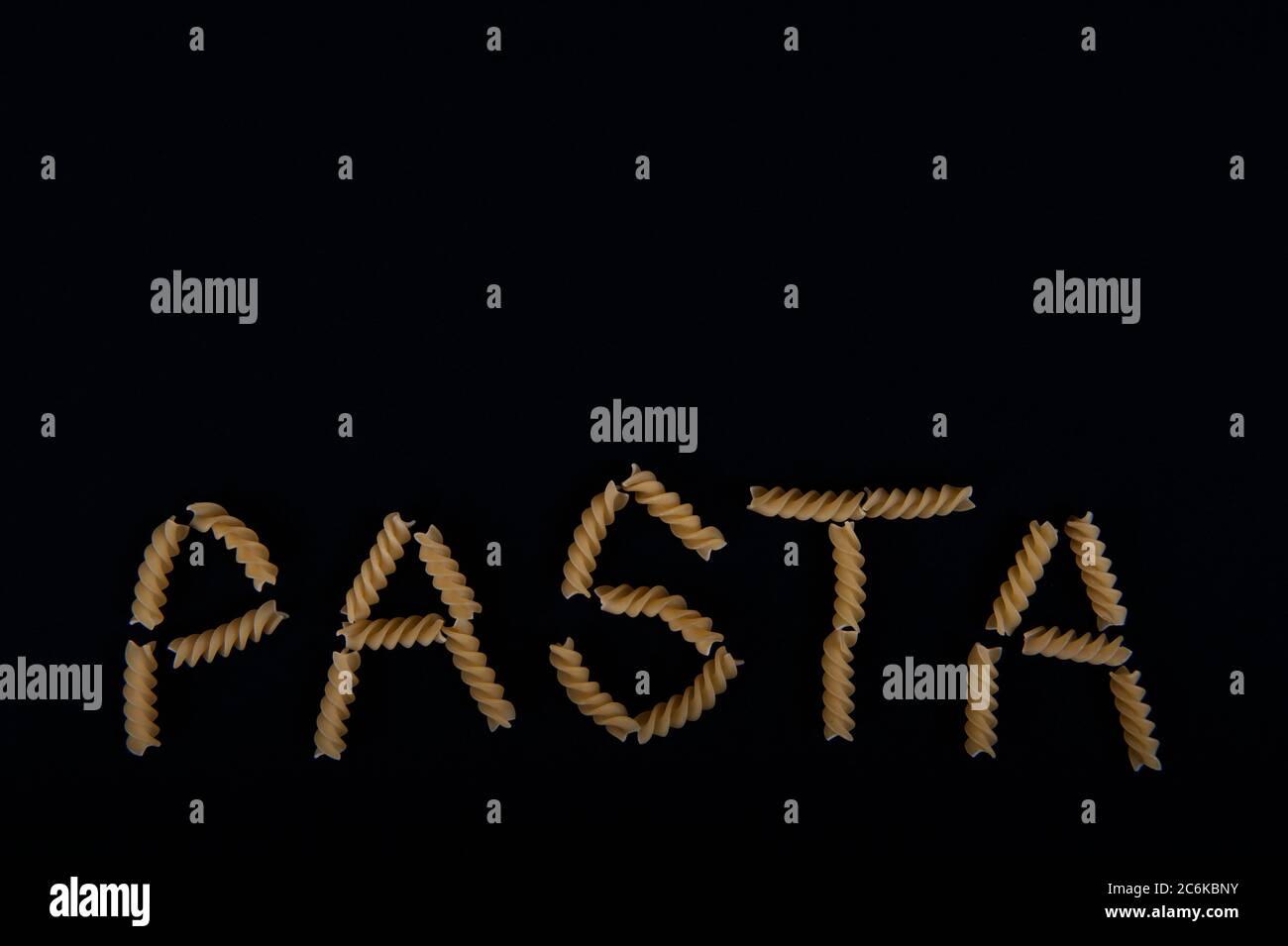 Das Wort Pasta mit Pastaschrauben geschrieben. Kopieren Sie den Platz im oberen Teil des horizontalen Bilds. Schwarzer Hintergrund. Stockfoto