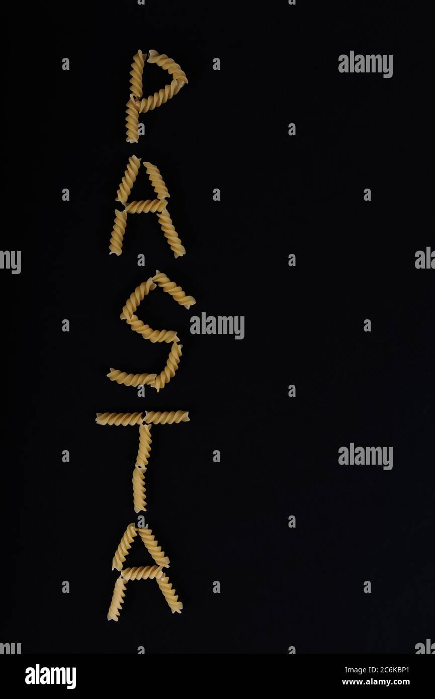 Das Wort PASTA vertikal in Pastaschrauben auf schwarzer Oberfläche geschrieben. Vertikale Aufnahme mit hohem Winkel und Kopieplatz im rechten Teil des Bildes. Stockfoto