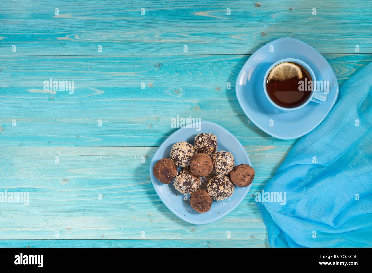 Eine Portion hausgemachte Energiebälle und eine Tasse Tee mit Zitrone auf einem blauen Holztisch. Leckeres und gesundes Dessert. Lifestyle. Die Aussicht von oben Stockfoto