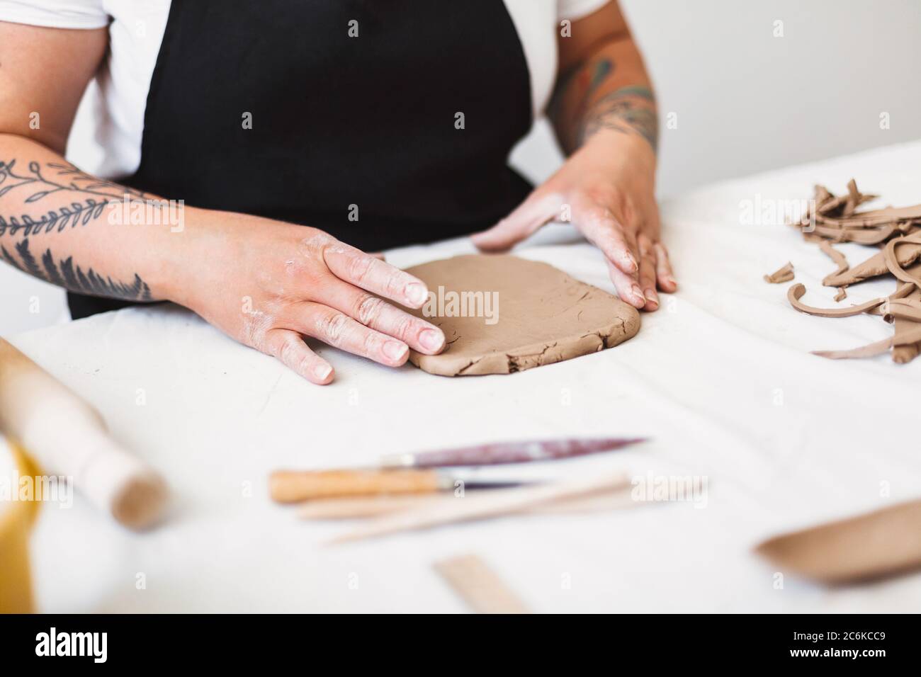 Nahaufnahme Frau Hände mit Tattoo in schwarzer Schürze arbeiten mit Ton in Töpferei. Stockfoto