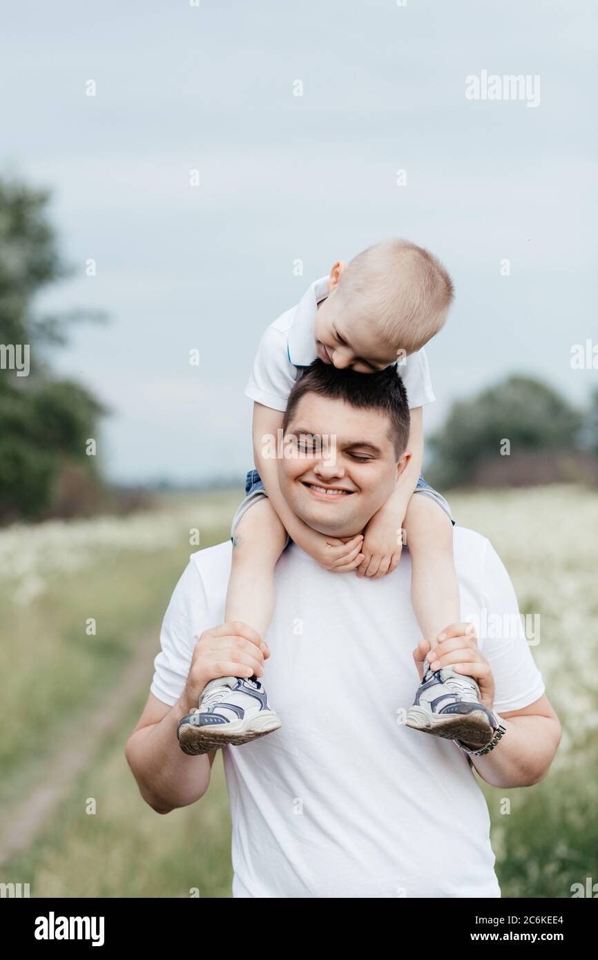 Glücklicher Vater hält seinen lächelnden kleinen Sohn auf den Schultern, während er in der Natur ist. Vater und Sohn. Frohe Familie Stockfoto