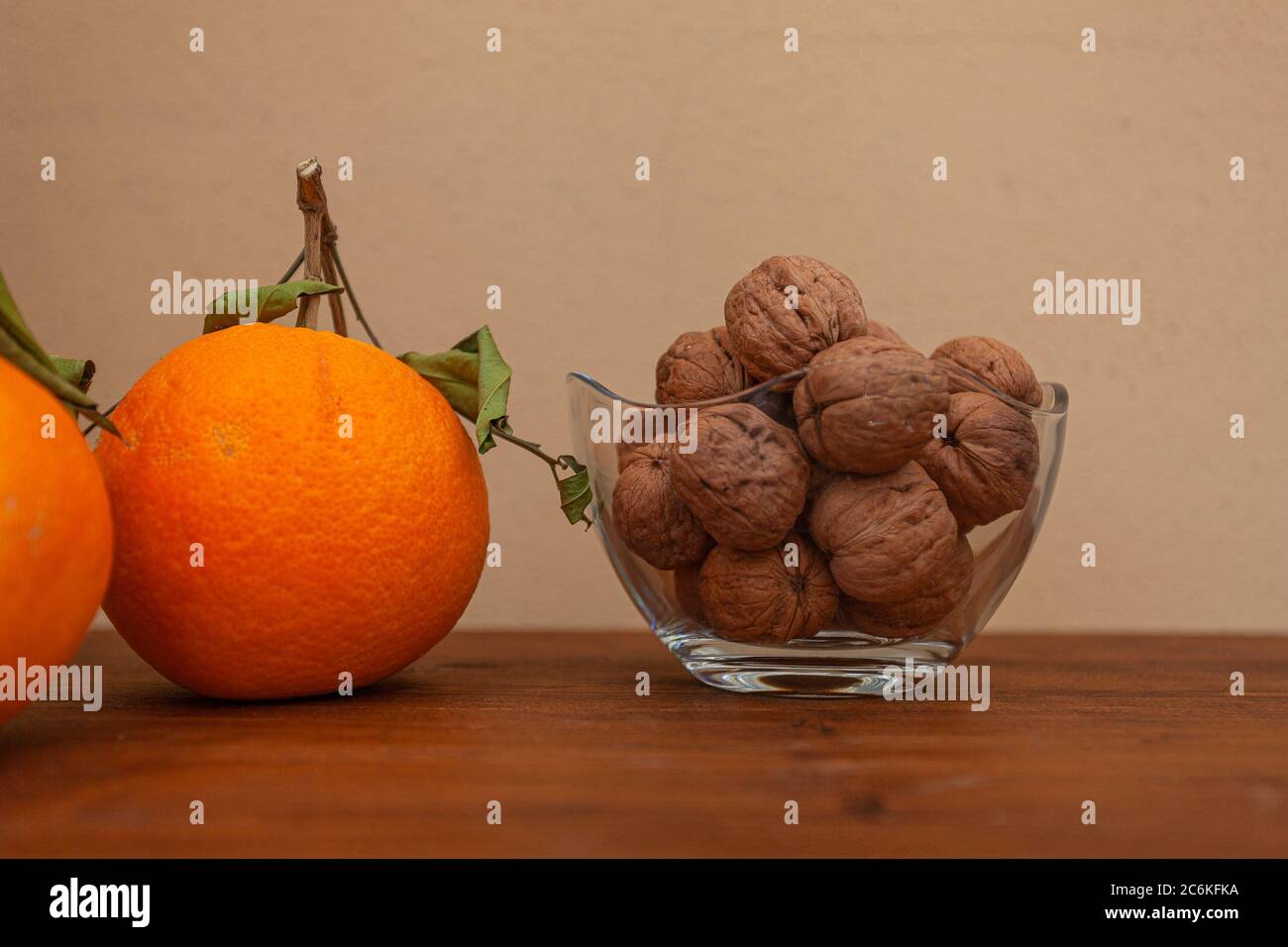 Orange mit zerknitterten Blättern und Glas voller Walnüsse auf Holztisch. Vorderansicht und Platz für Text Stockfoto