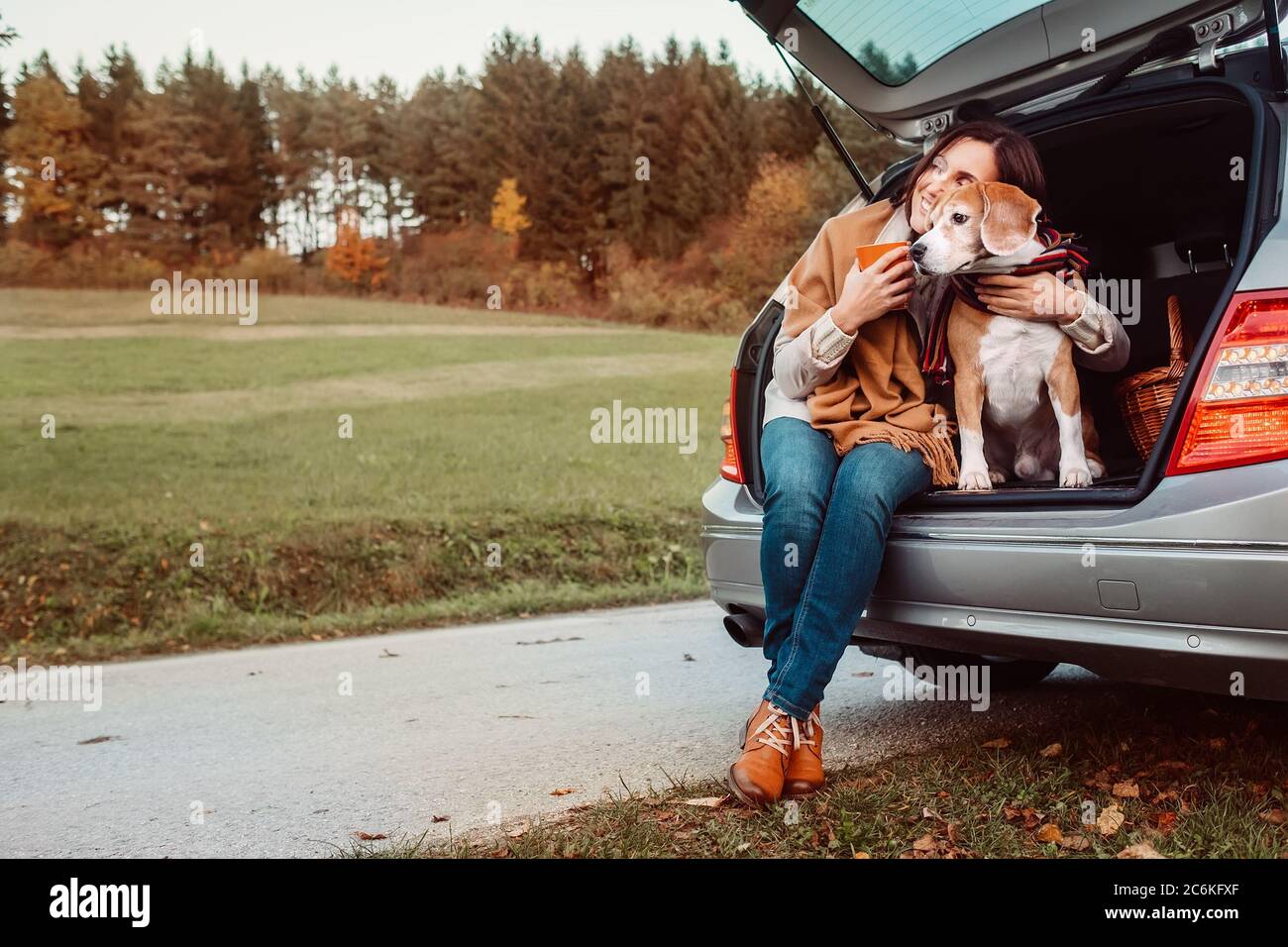 Eine Frau mit Hund sitzt zusammen in einem LKW und wärmt heißen Tee. Auto travel with pets Concept Bild. Stockfoto