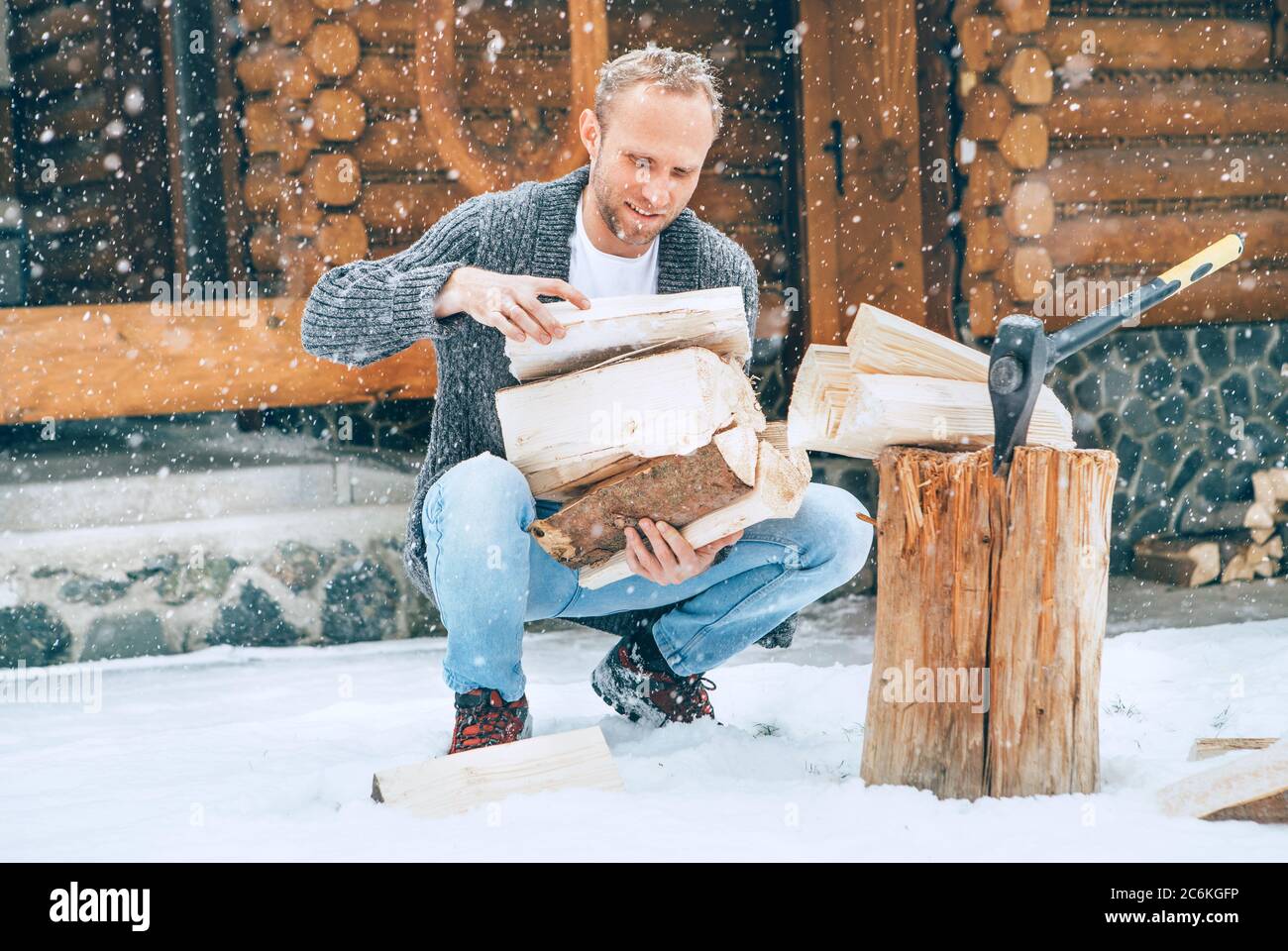 Mann sammelt gehacktes Brennholz auf verschneiten Hof für ein Haus Kamin mit schweren Schneeflocken Hintergrund. Winter Landurlaub Konzept Bild Stockfoto