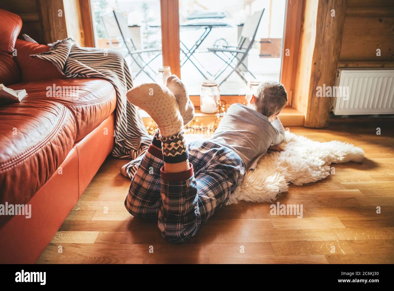 Junge auf dem Boden auf Schaffell liegen und im Fenster schauen, in gemütlichen Hause Pyjama und warme Socken gekleidet Stockfoto