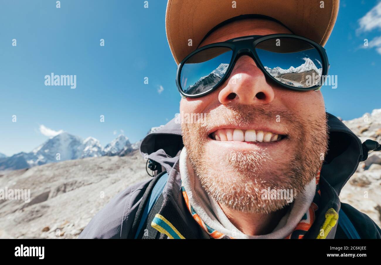 Ultra-Weitwinkel-Porträtaufnahme des Berges in großer Höhe lächelnd unrasiert glücklich Wanderer in Baseball-Cap mit Schneespitzen und Bergkette neben h Stockfoto