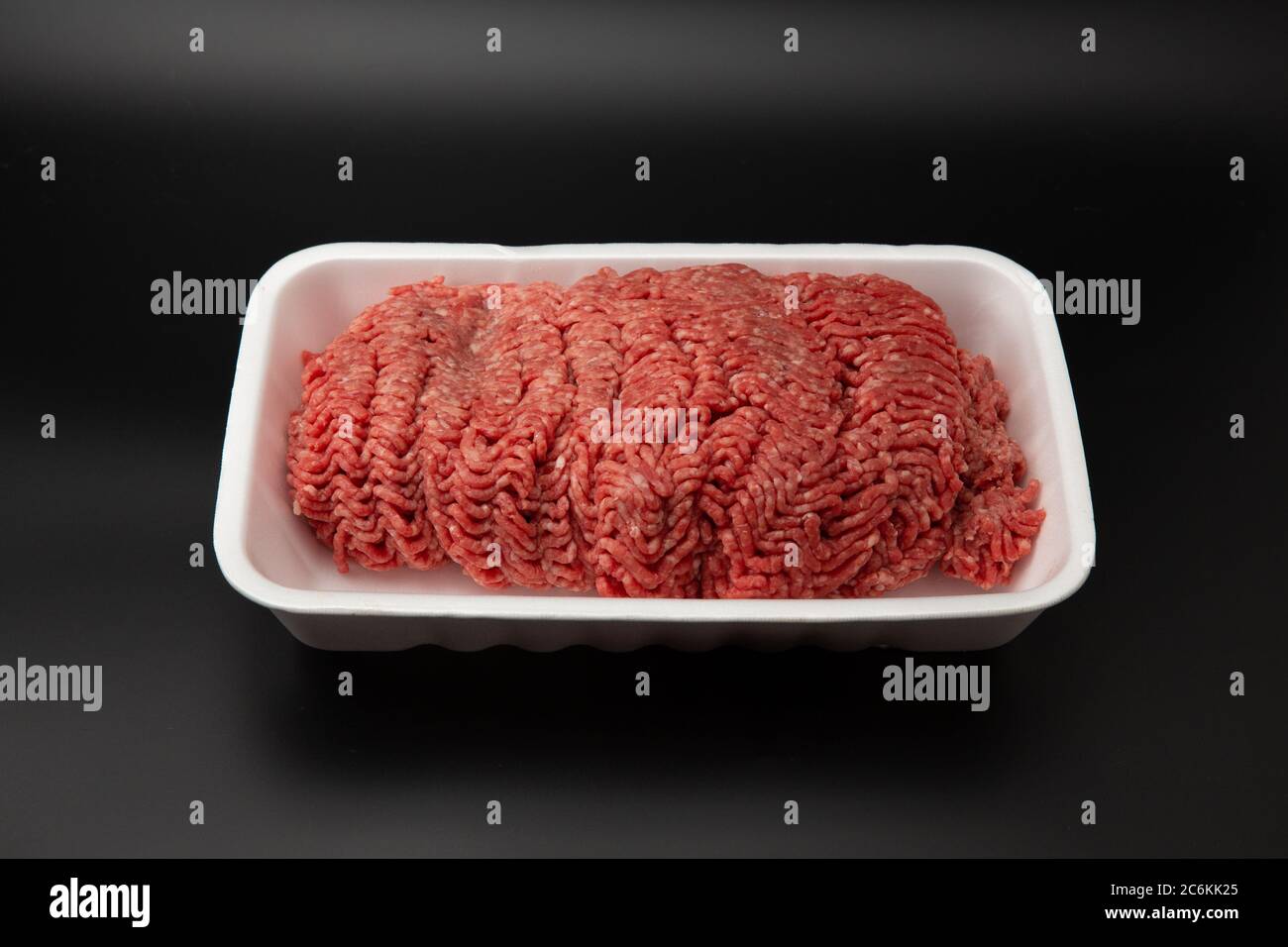 Rohes Hackfleisch (gemahlen) in einem weißen Styroporbehälter, isoliert auf schwarzem Hintergrund mit Platz für Text Stockfoto