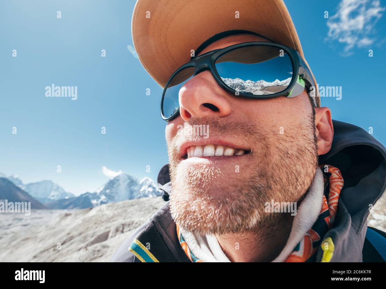 Ultra-Weitwinkel-Porträtaufnahme des Berges in großer Höhe lächelnd unrasiert glücklich Wanderer in Baseball-Cap mit Schneespitzen und Bergkette neben h Stockfoto