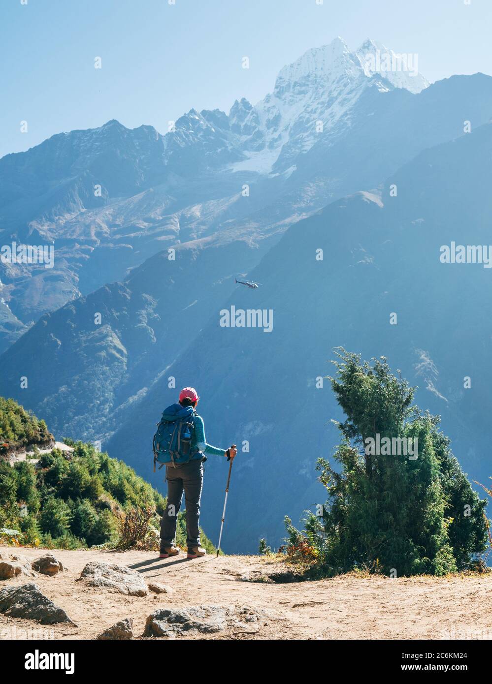 Junge Wanderer Backpacker Frau mit Trekking Stöcke genießen die Thamserku 6608m Berg mit fliegenden Rettungshubschrauber in der Höhe Acclimatiza Stockfoto