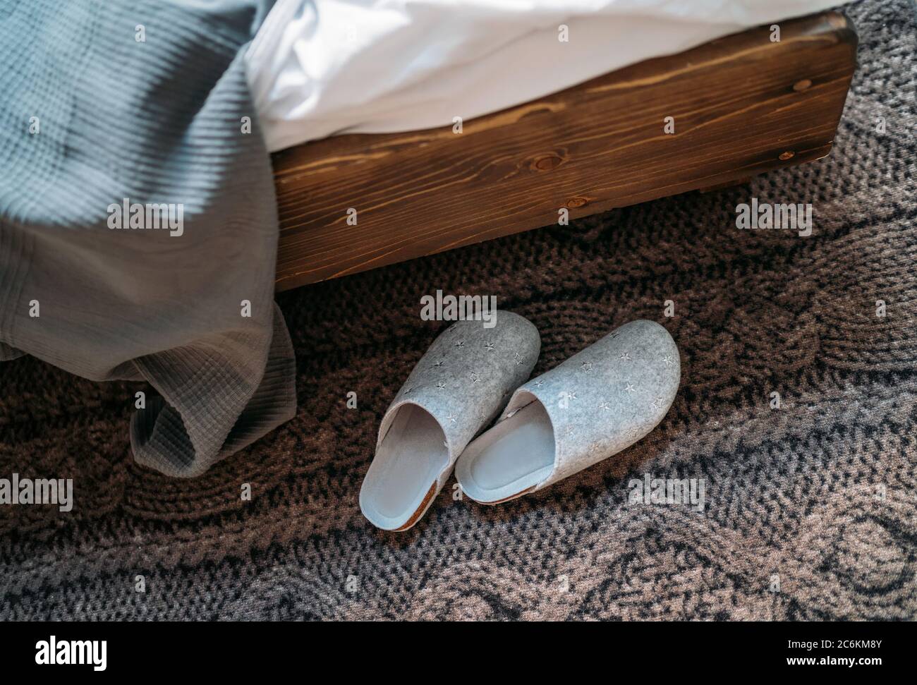 Das Paar graue Hausschuhen in der Nähe des Holzbettes auf dem "Strickboden" im gemütlichen Schlafzimmer. Home Sweet Home Konzept Bild. Stockfoto