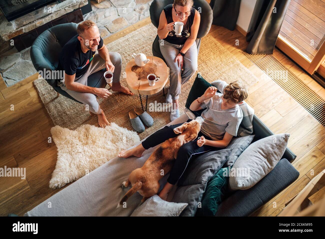 Gemütliche Familie Tee Zeit. Vater, Mutter und Sohn im Wohnzimmer. Junge liegt auf einem bequemen Sofa und streichelt ihren Beagle Hund und lächelt. Frieden Stockfoto