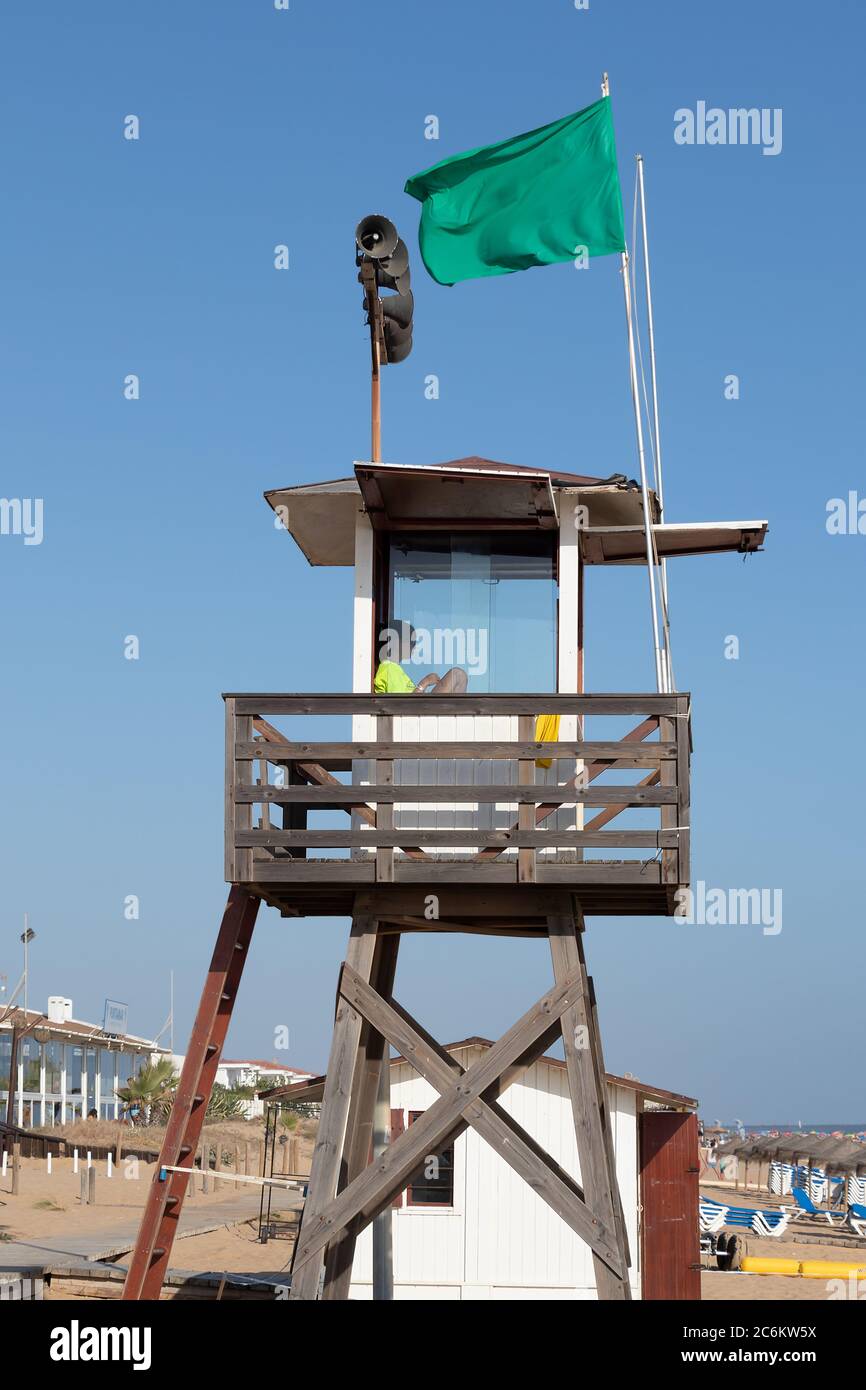 Punta Umbria, Huelva, Spanien - 9. Juli 2020: Ein Rettungsschwimmer sitzt auf einem Überwachungsturm am Strand von Punta Umbria, Huelva, Spanien Stockfoto