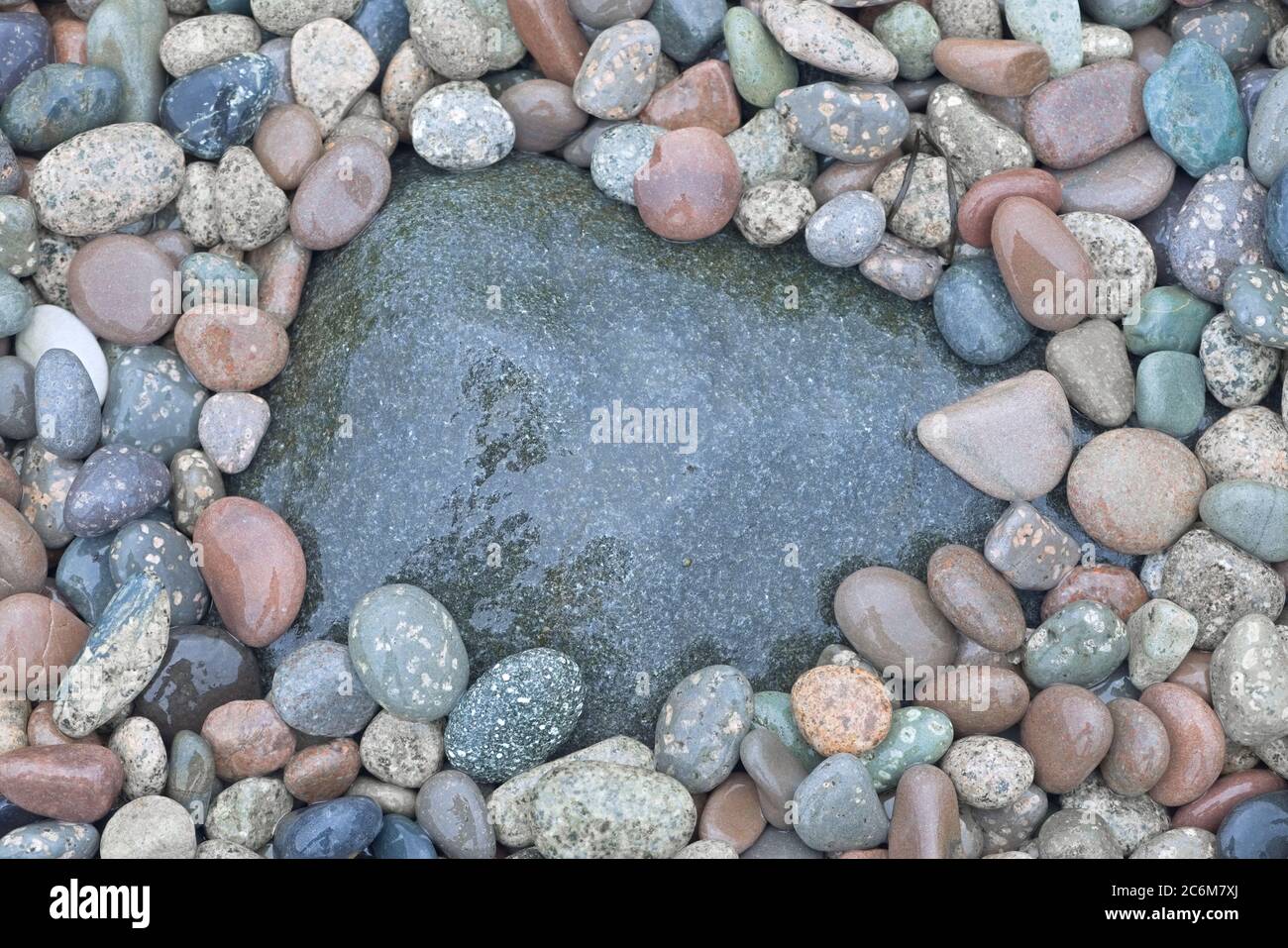 2 - ein großer, nasser und dunkler Stein, umgeben von vielen helleren Kieselsteinen, tolle Hintergrundstruktur mit Kopierraum. Stockfoto