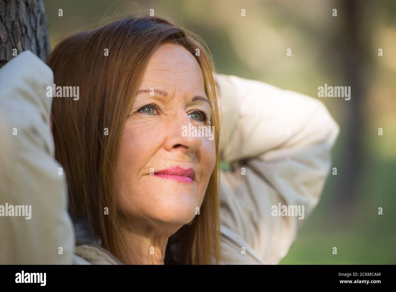 Portrait Attraktive reife Frau mit langen Haaren posiert glücklich entspannt, nachdenklich und zuversichtlich im Freien im Park, freundlich lächelnd. Stockfoto