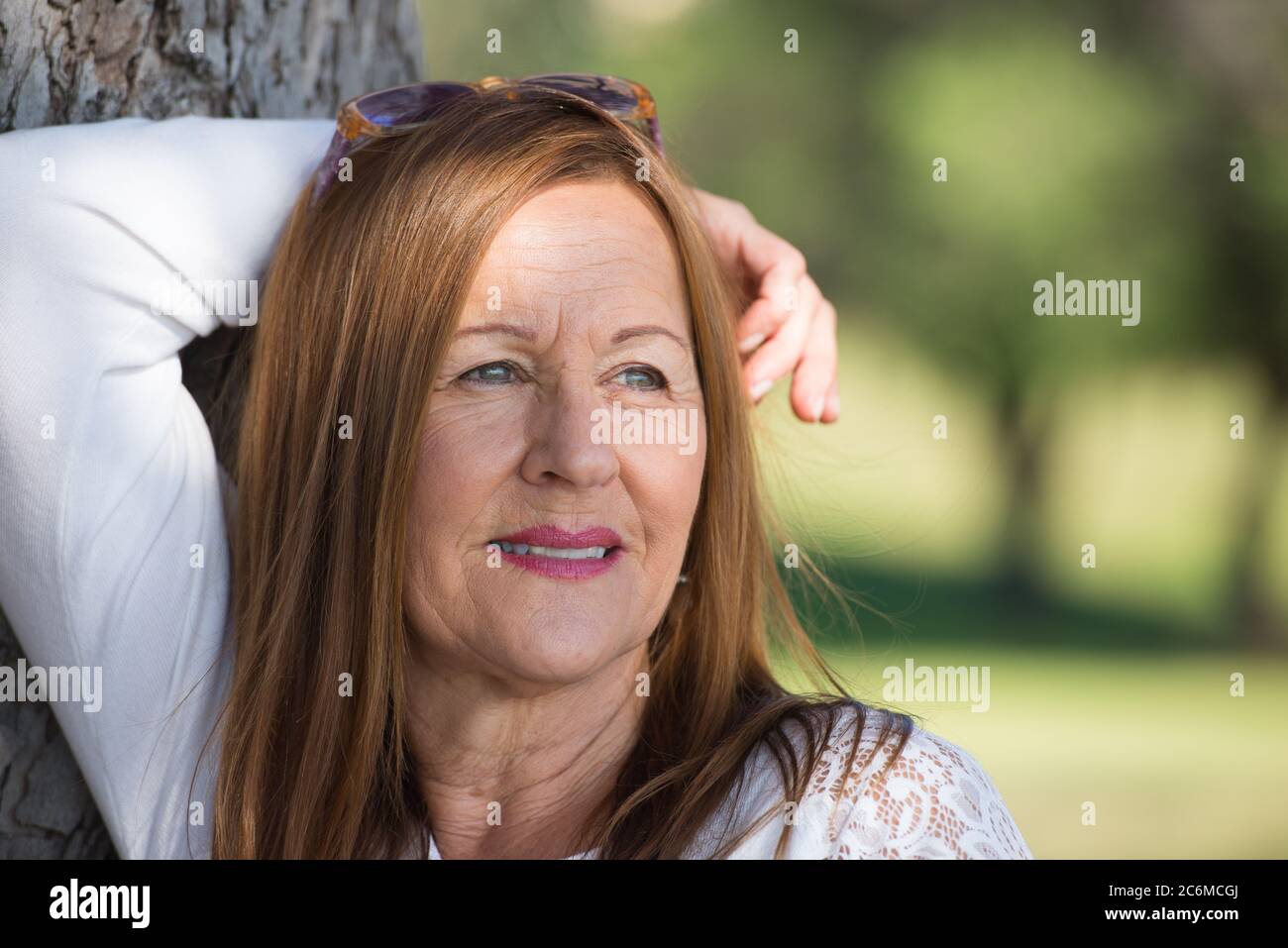 Portrait Attraktive reife Frau mit langen Haaren posiert glücklich entspannt, nachdenklich und zuversichtlich im Freien im Park, freundlich lächelnd. Stockfoto