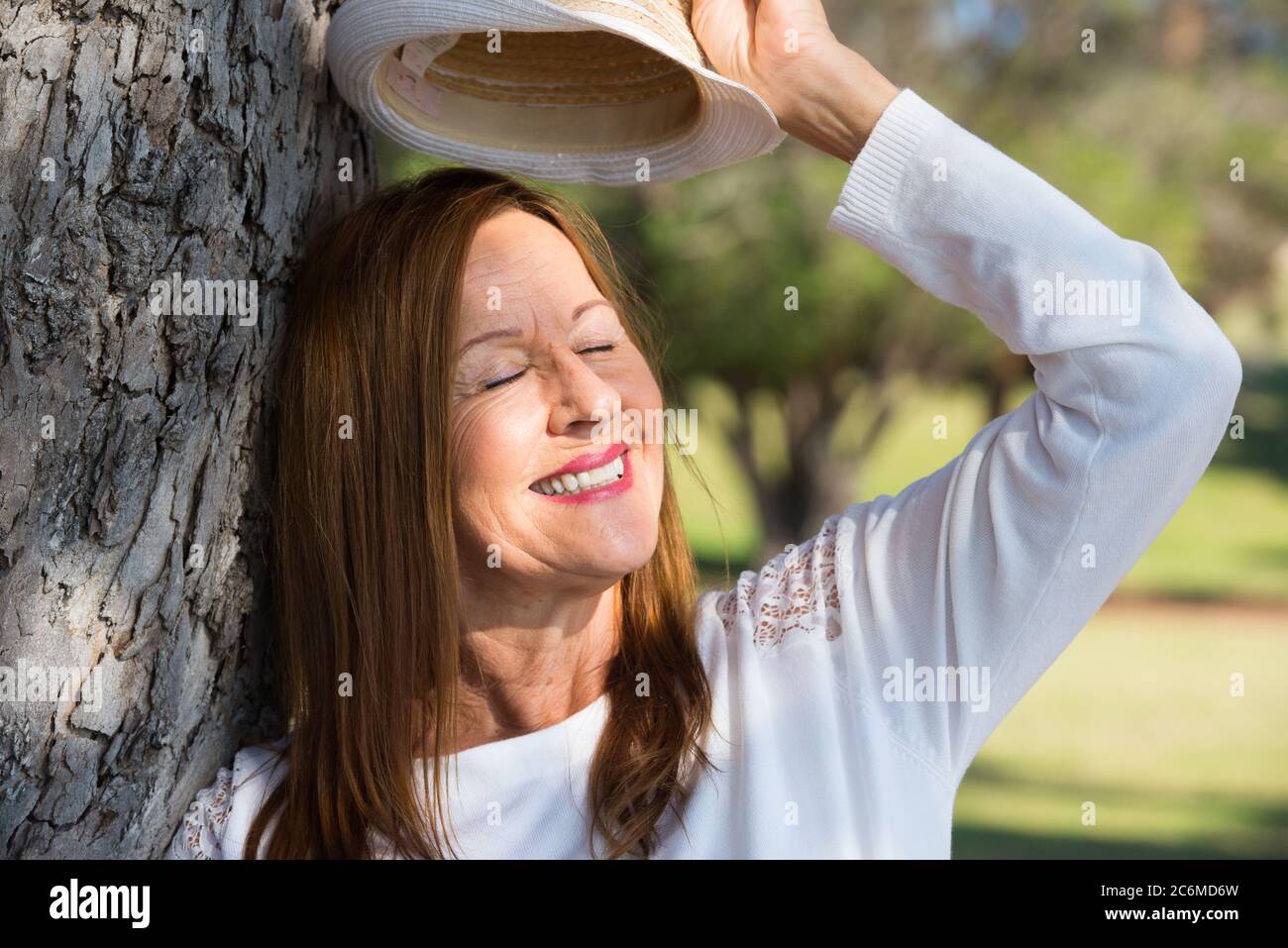 Portrait glücklich entspannt und attraktiv reife Frau posiert freundlich lächelnd und geschlossenen Augen mit Hut im Park im Freien. Stockfoto
