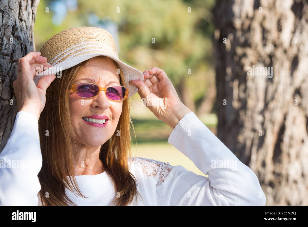 Portrait Attraktive reife Frau im Park, glücklich entspannt und selbstbewusst, trägt Sonnenbrille und Hut am sonnigen Sommertag. Stockfoto
