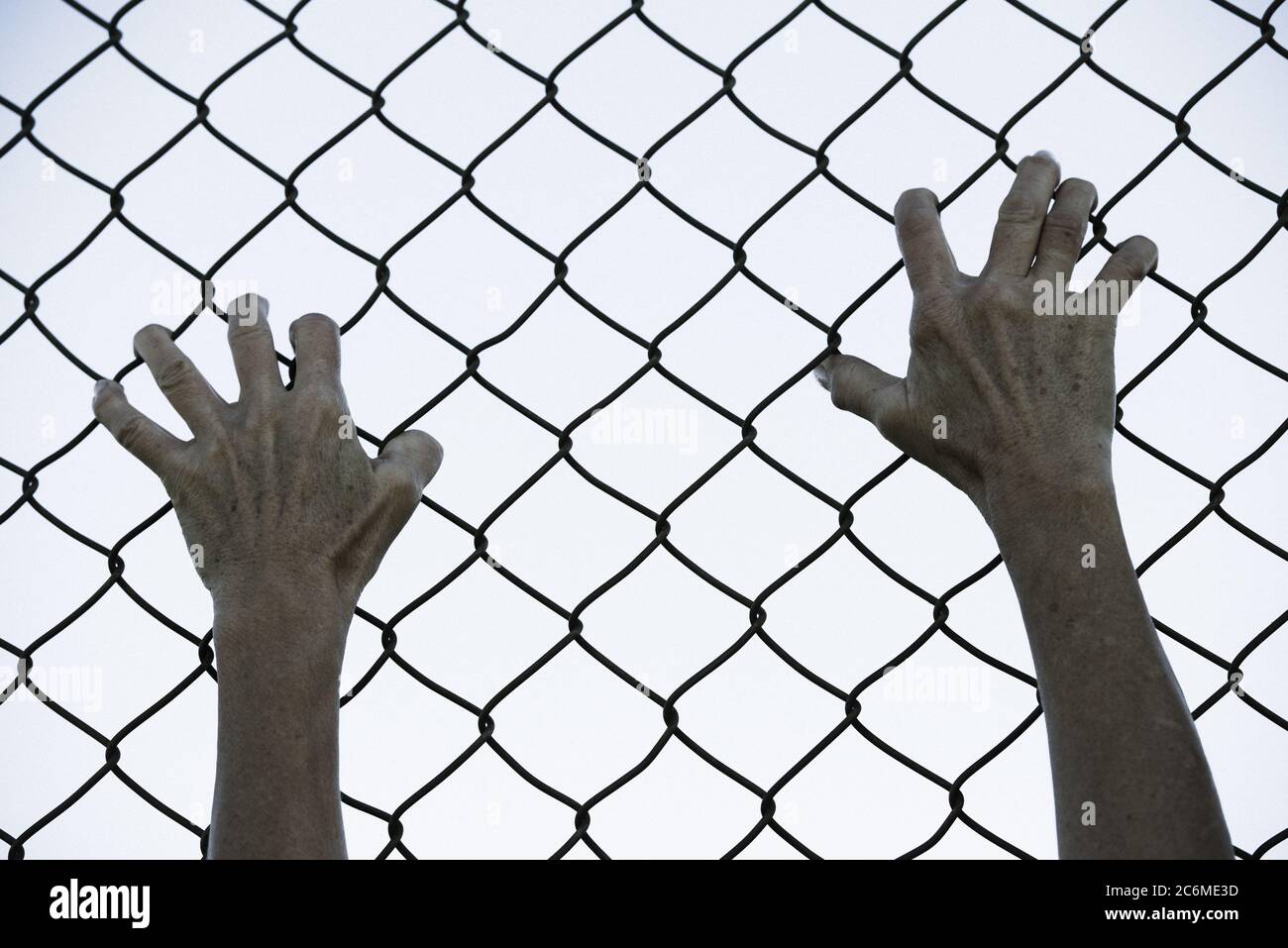 Gebleicht gefiltertes Bild von Händen in verzweifeltem Griff auf Netz verdrahteten Zaun, symbolisiert Gefangenschaft, hoffnungslos, Entführung, Kampf und gestresste Person. Stockfoto