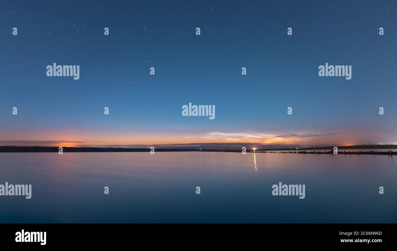 Natürliche Nachtlandschaft mit einem Sternenhimmel auf dem See, vor der Dämmerung der Sonne in der Ferne lila Wolken. Stockfoto