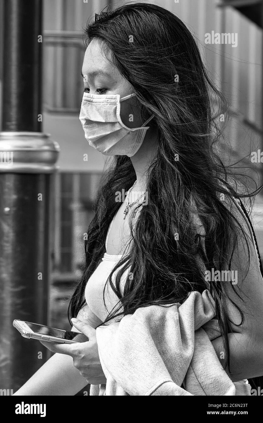 Mädchen mit Gesichtsmaske mit Handy während covid 19 Pandemie, Sukhumvit, Bangkok, Thailand Stockfoto