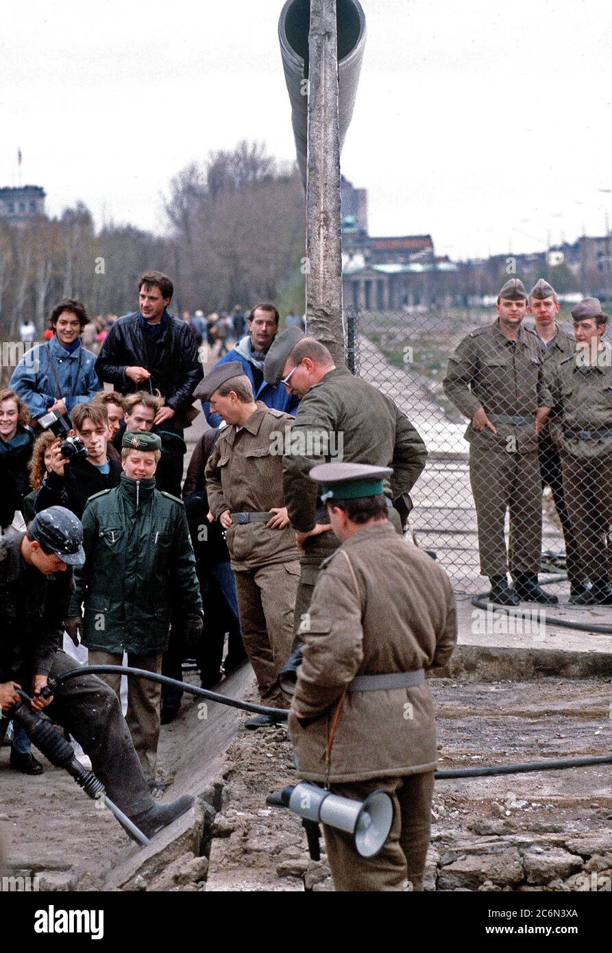 Polizei- und Westdeutschen Bürger beobachten, wie ein Handwerker einen Abschnitt der Berliner Mauer zerlegt am Potsdamer Platz. Stockfoto